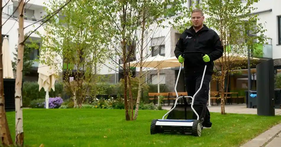 Grünflächenpflege, Reinigung und Pflege von Grünanlagen und Außenflächen. Mitarbeiter des Immobilienservice Mauss mäht einen Rasen im Rahmen des Facility Managements.