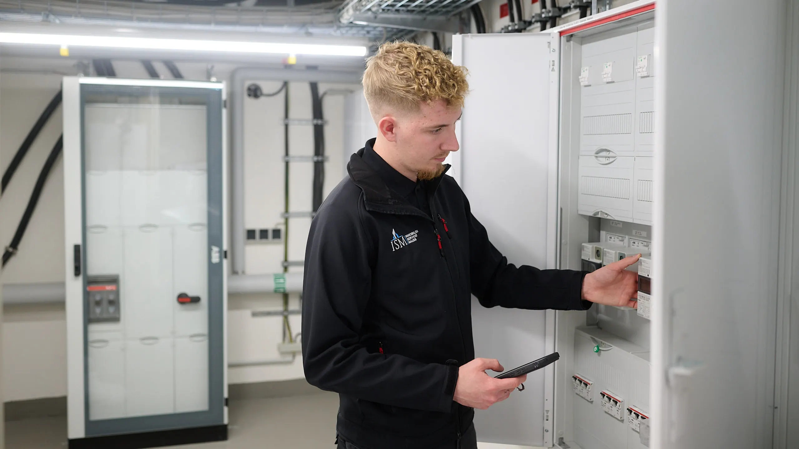Infrastrukturelles Facility Management durch einen Mitarbeiter des Immobilienservice Mauss. Mitarbeiter kontrolliert einen Stromkasten. Gebäudedienste, Hausmeisterdient und Grünflächenpflege für Gewerbekunden.